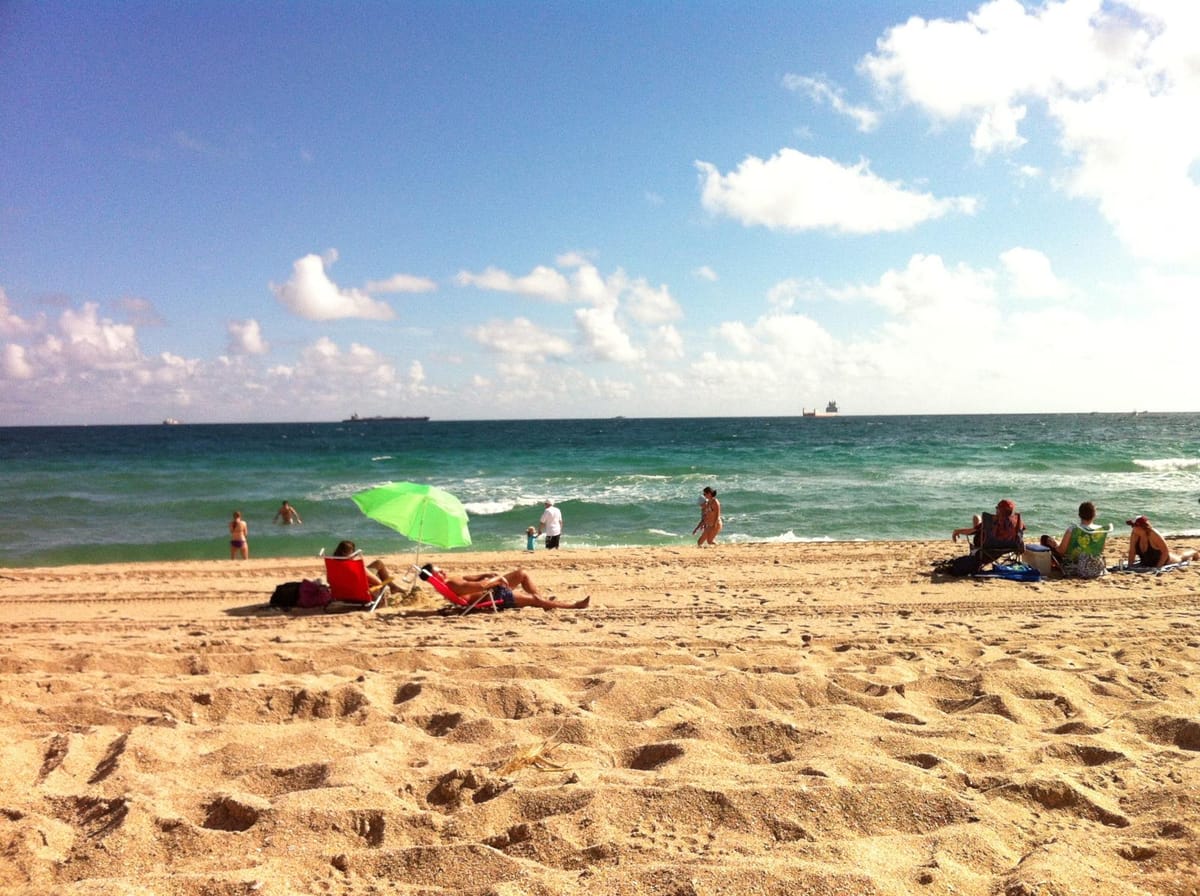 A photo of a beach with people swimming and sunbathing in beach chairs. 